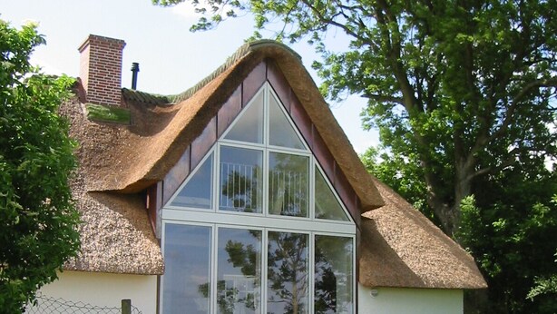Ein Haus mit einem Reetdach, einem großen Glasfenster und einem Ziegelkamin.