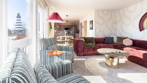 A modern living room with striped sofas, a red sofa, and a round coffee table. - Base Camp – Modern Cozy Retreat with Sauna, Hot Tub & Fun for Families in WDM (West Des Moines)
