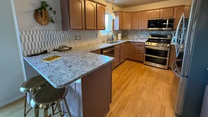 A modern kitchen with wooden cabinets, granite countertops, and stainless steel appliances. - Base Camp – Modern Cozy Retreat with Sauna, Hot Tub & Fun for Families in WDM (West Des Moines)