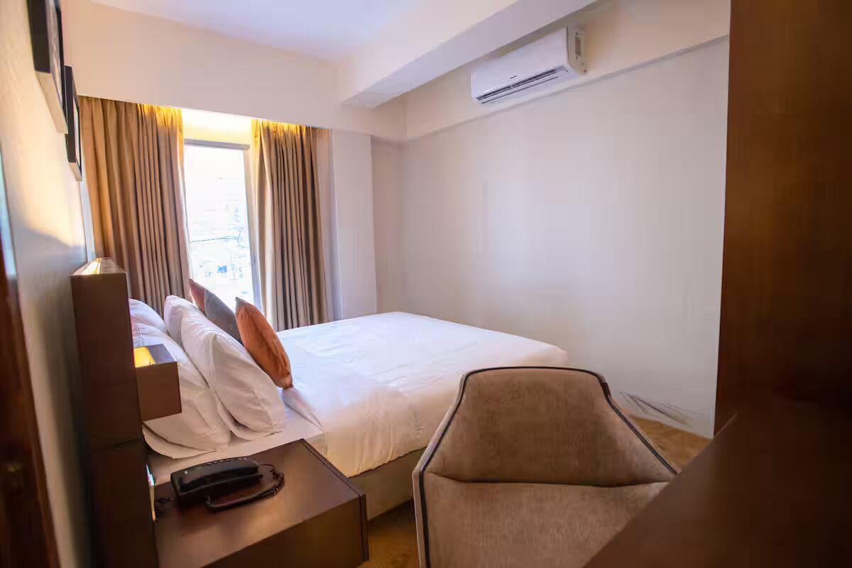 Une chambre d’hôtel équipée d’un lit, d’une chaise, d’un bureau avec une lampe et d’un appareil de climatisation.