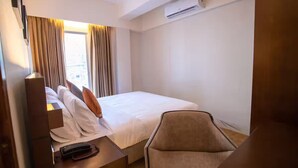 A hotel room with a bed, a chair, a desk with a lamp, and an air conditioning unit. - Jatra Flagship Rajshahi City Centre 4 (Rajshahi)
