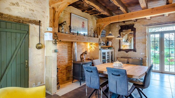 Een rustieke eethoek met een houten tafel, stoelen en een bakstenen muur.