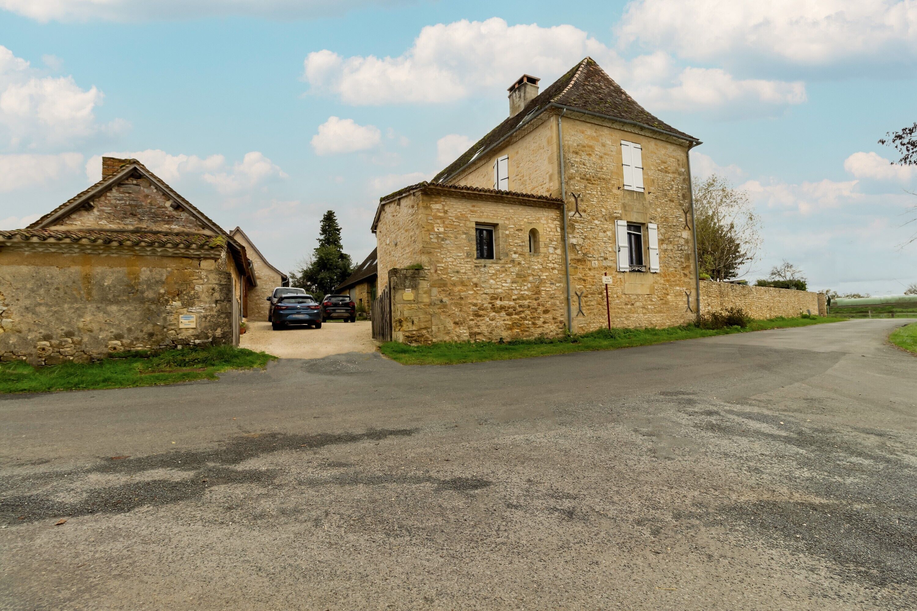 Un bâtiment en pierre avec une route pavée devant, une voiture garée et un ciel dégagé.