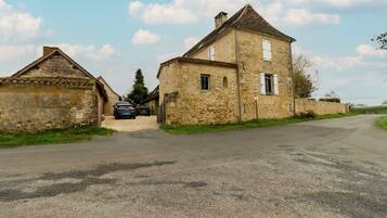 A stone building with a paved road in front, a parked car, and a clear sky.