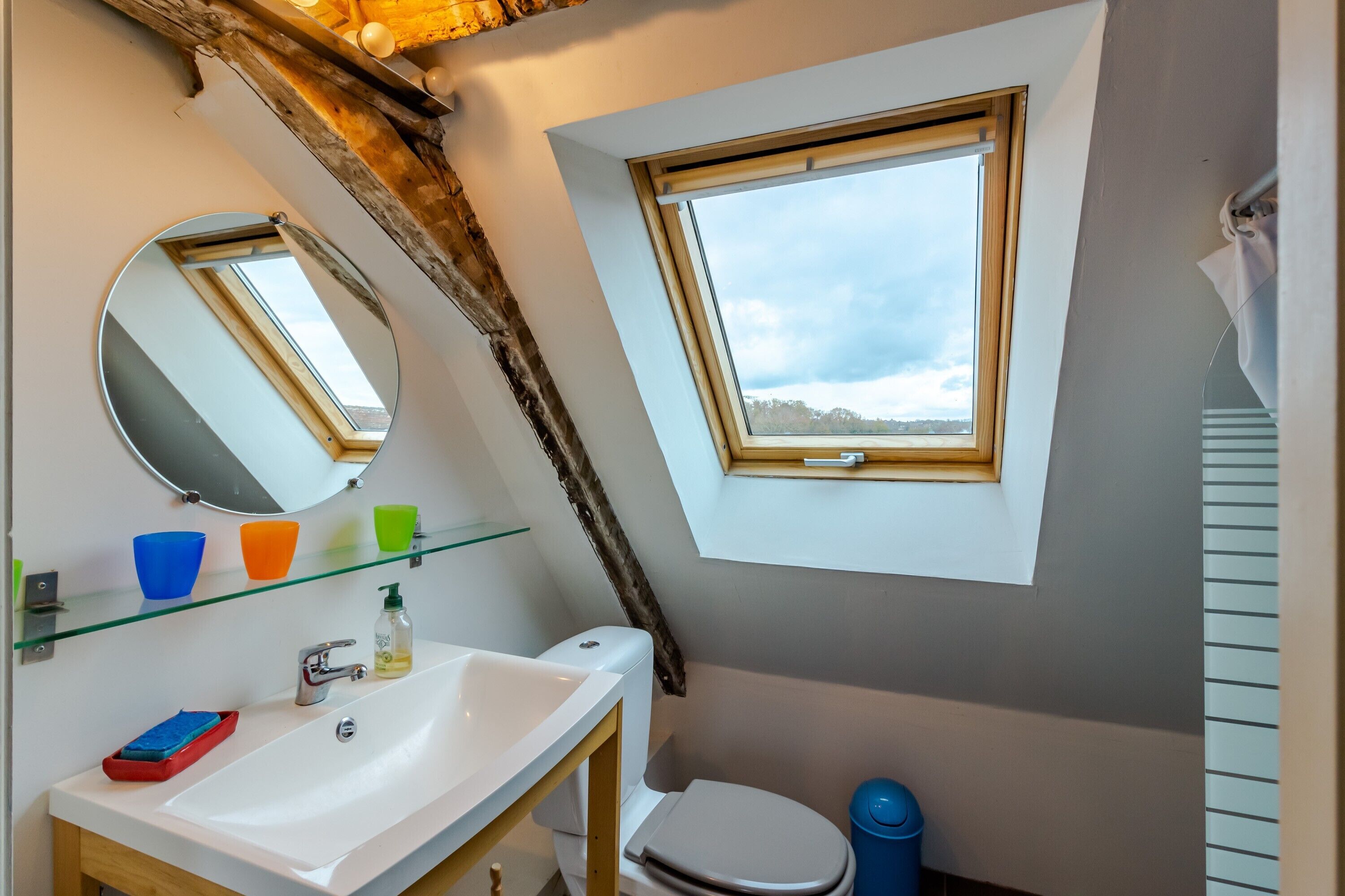 Een badkamer met dakraam, spiegel, wastafel en toilet.