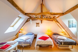 A cozy attic bedroom with two beds, a small table, and a window.