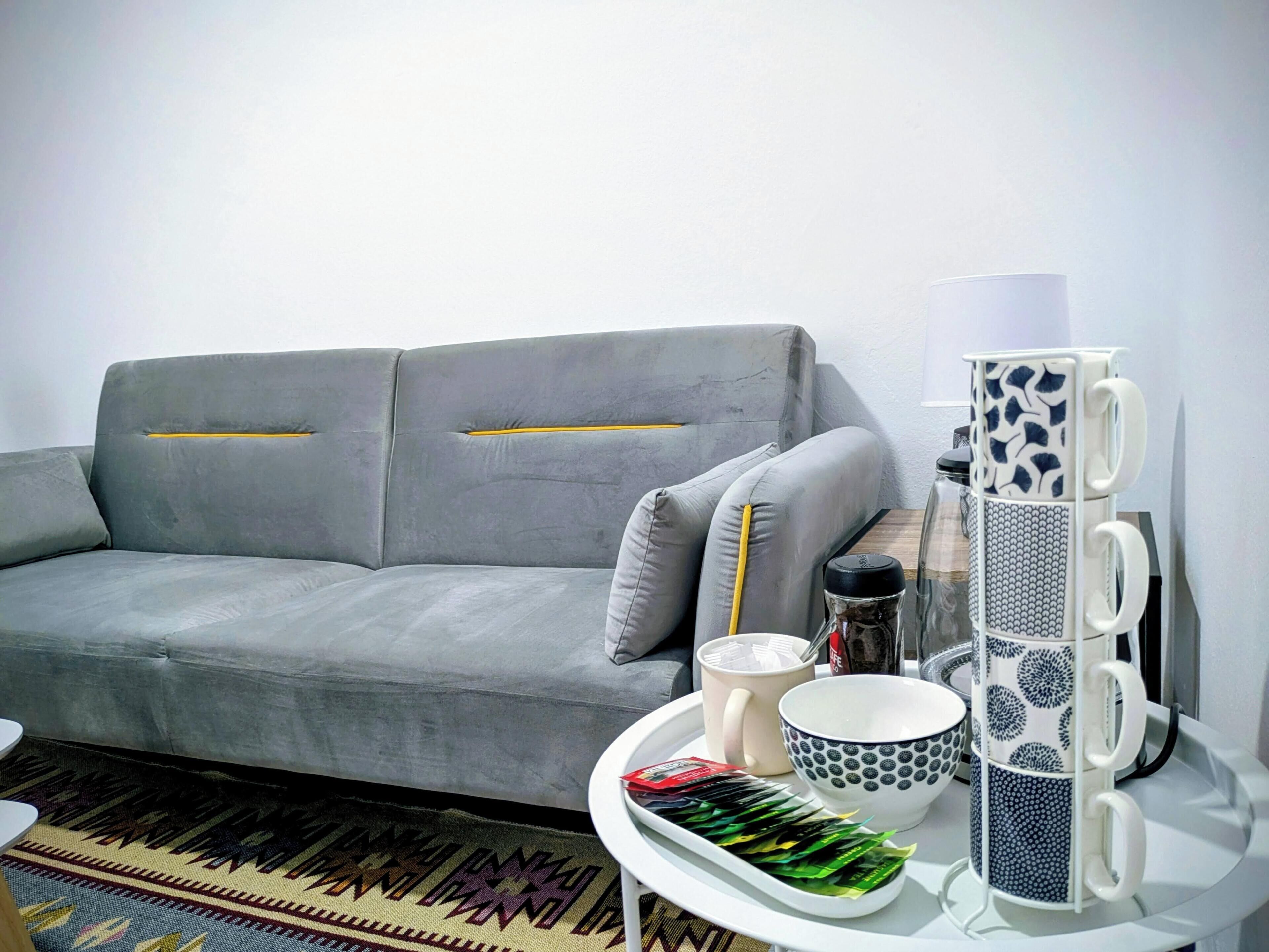 A modern living room with a grey sofa, a patterned rug, and a tray with tea bags and cups.
