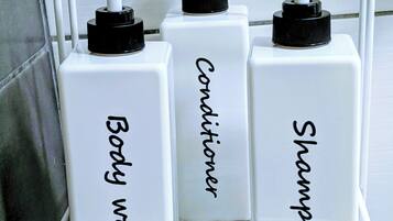 A bathroom shelf with three white bottles labeled "Body wash," "Conditioner," and "Shampoo."