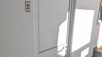 A white door with a number '2' sign, a window casting a shadow, and a small set of steps leading to a door.