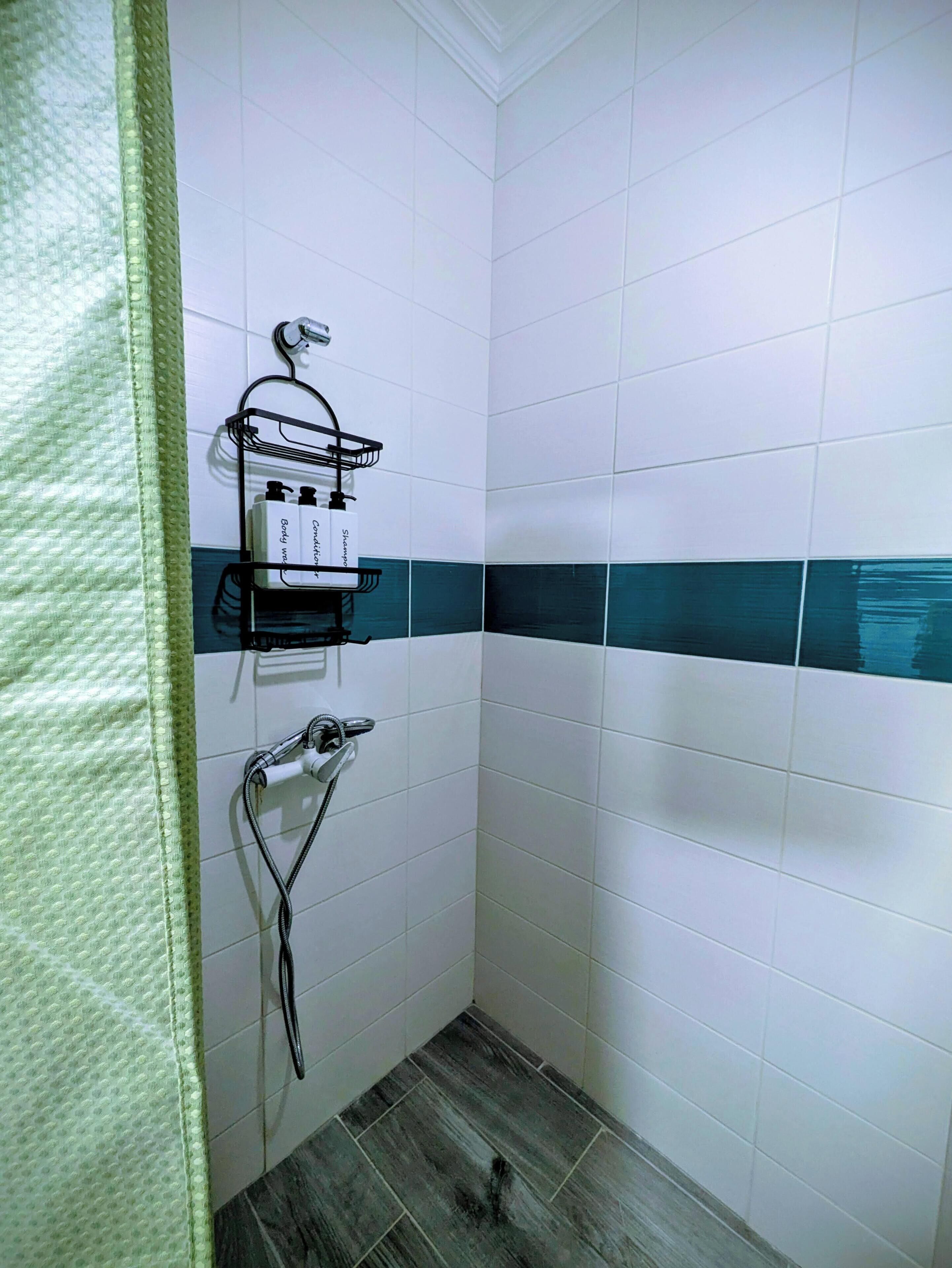 Een badkamer met witte en teal tegels, een douche met handdouche, en een handdoekrek met flesjes.