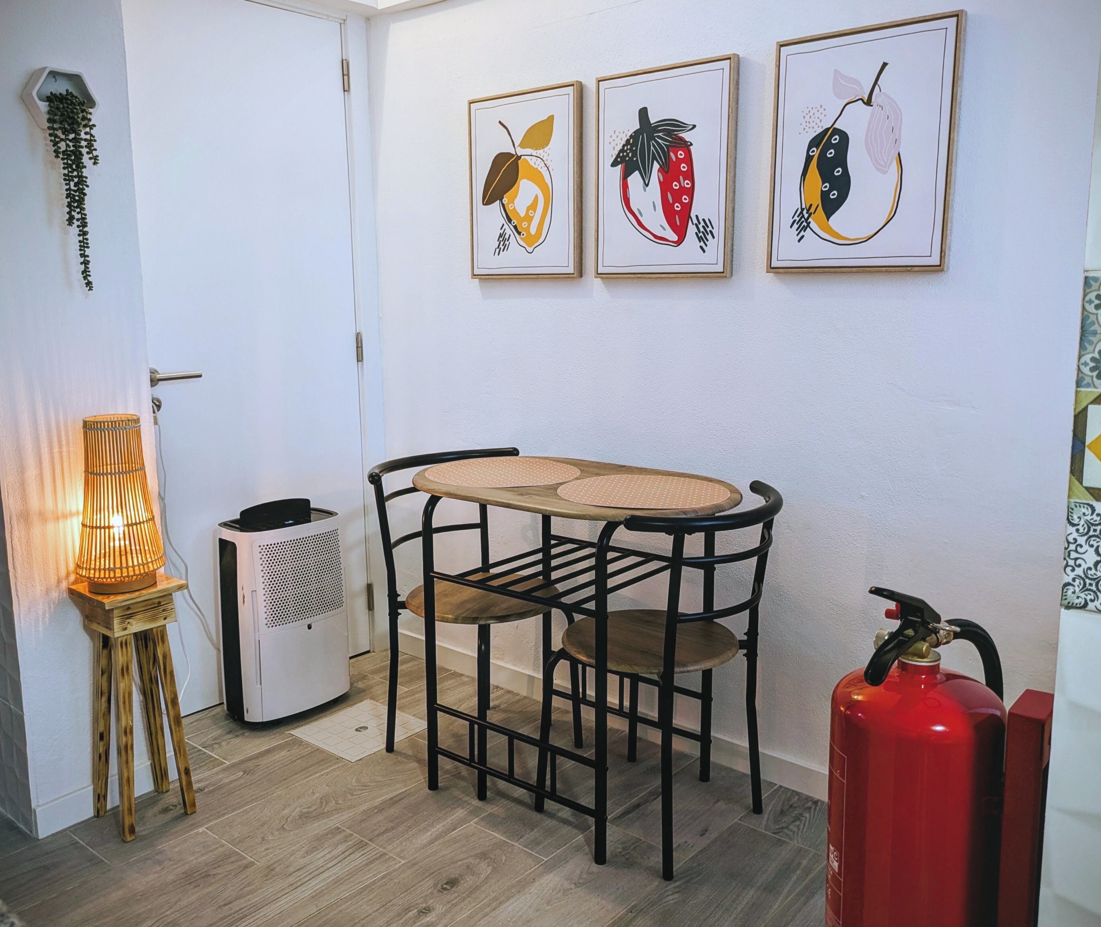 A small dining area with a table and chairs, a hanging plant, a wall-mounted air purifier, and a red fire extinguisher.