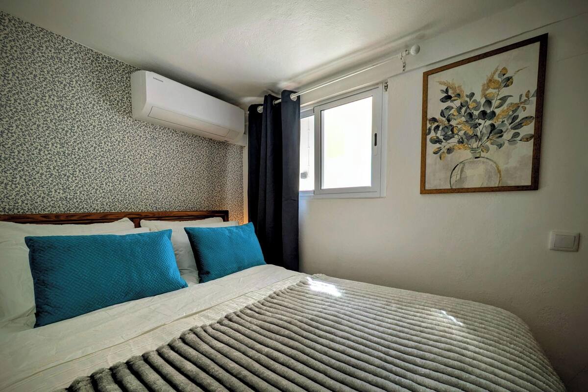 Un dormitorio con pared de diseño, una cama con almohadas azules, una manta gris y un cuadro de flores.