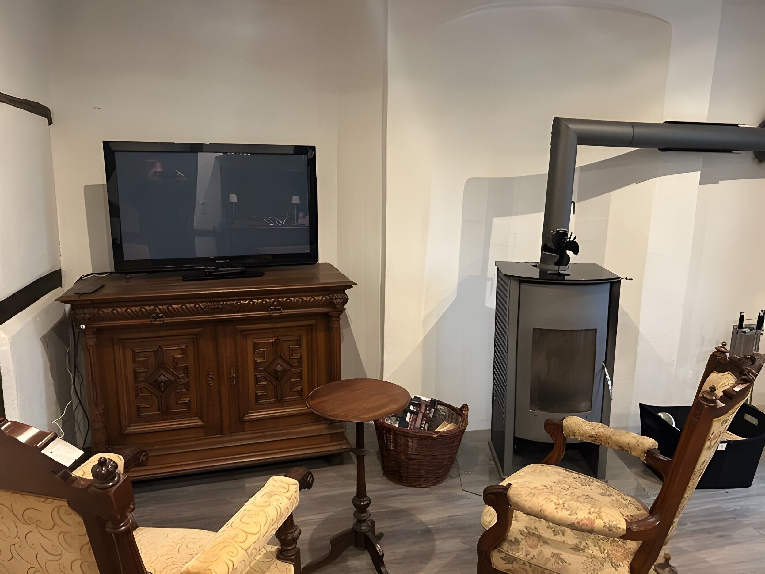 Olohuoneessa on televisio, joka on sijoitettu puiseen kaappiin, takka ja kaksi verhoiltua nojatuolia.