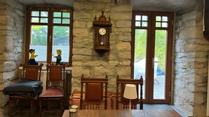 Una habitación rústica con paredes de piedra, muebles de madera, un reloj y ventanas grandes.
