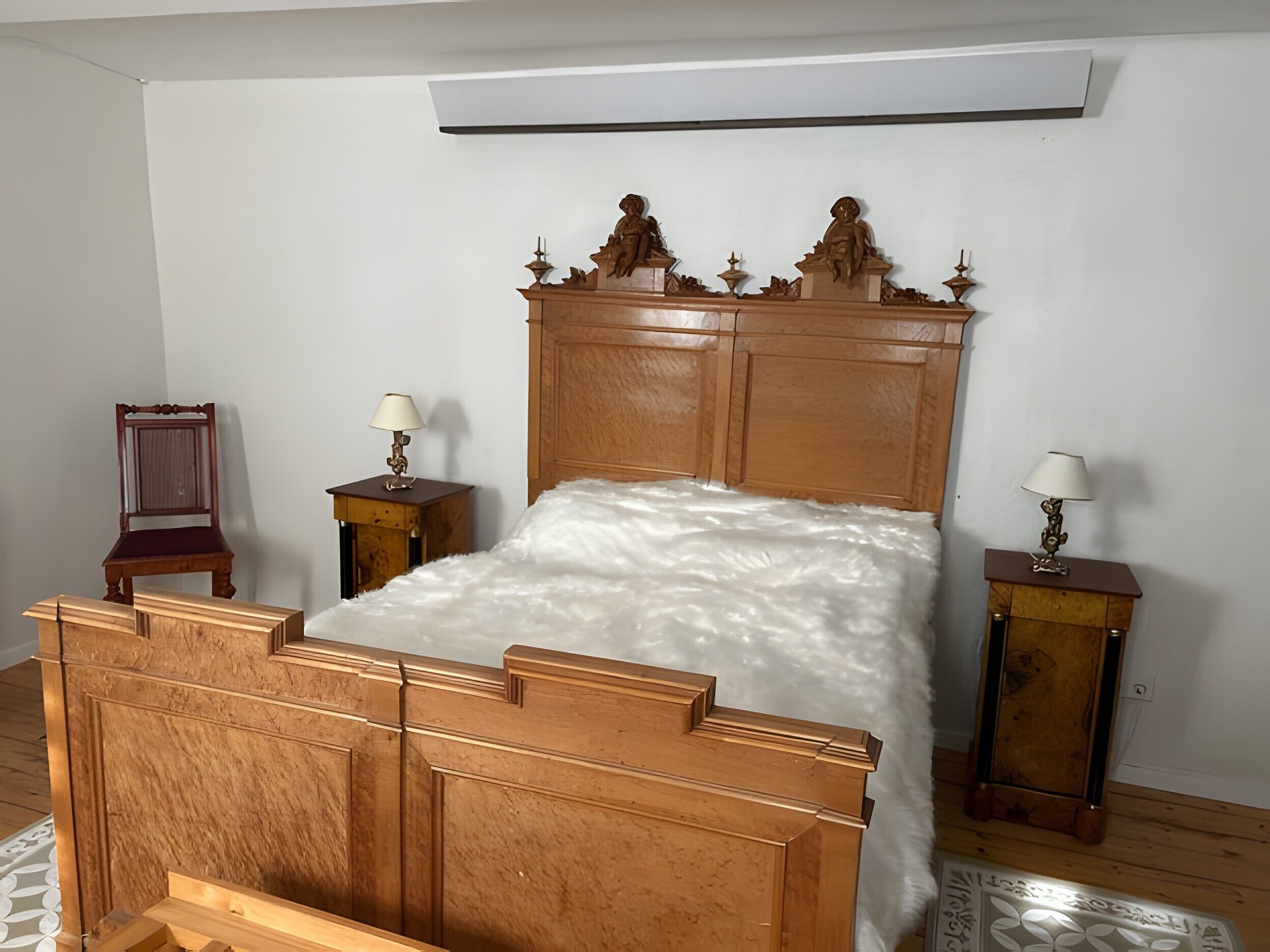 A bedroom with a wooden bed, two nightstands with lamps, a chair, and a wall-mounted air conditioner.