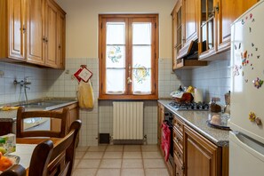 Eine Küche mit Holzausstattung, einem Fenster mit Vorhängen, einer gefliesten Spritzschutzwand und einem Kühlschrank mit Magneten.