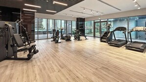 Ett modernt gym med olika typer av träningsutrustning, stora fönster och utsikt över stadsbilden.