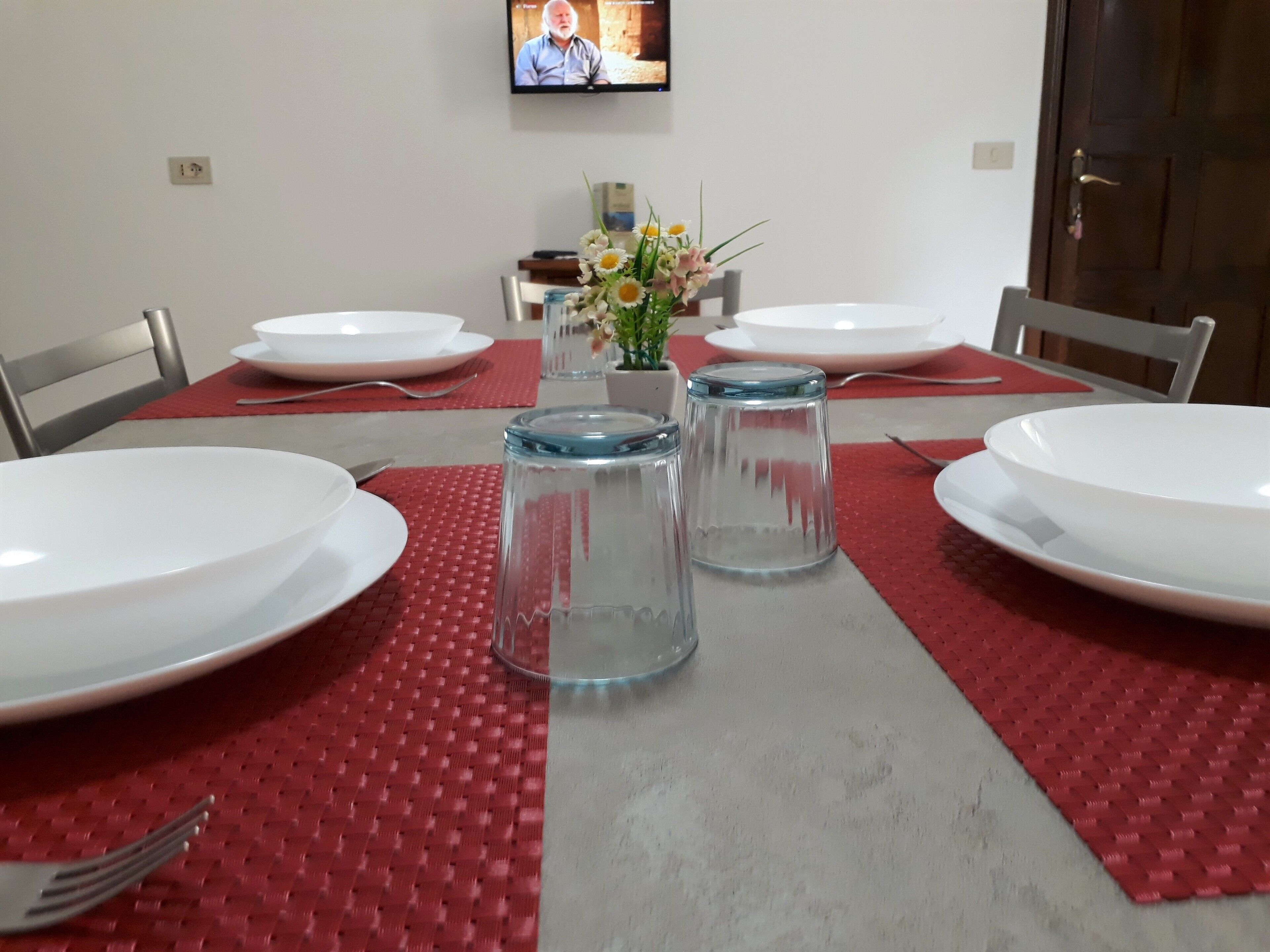 A dining table set with white plates, red placemats, and clear glass water glasses.