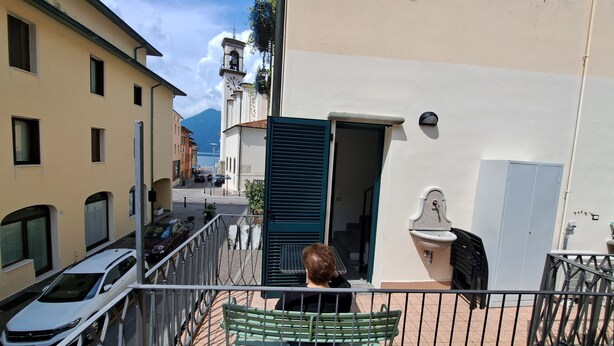 Ein Balkon mit Blick auf eine Straße, ein Gebäude mit einem Glockenturm und ein stehendes Auto.
