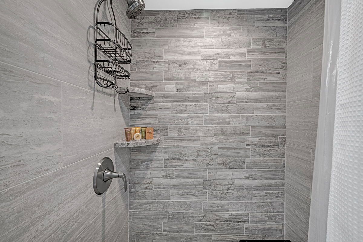 Ducha con pared de piedra gris, cabezal de ducha metálico y estante con artículos de aseo.