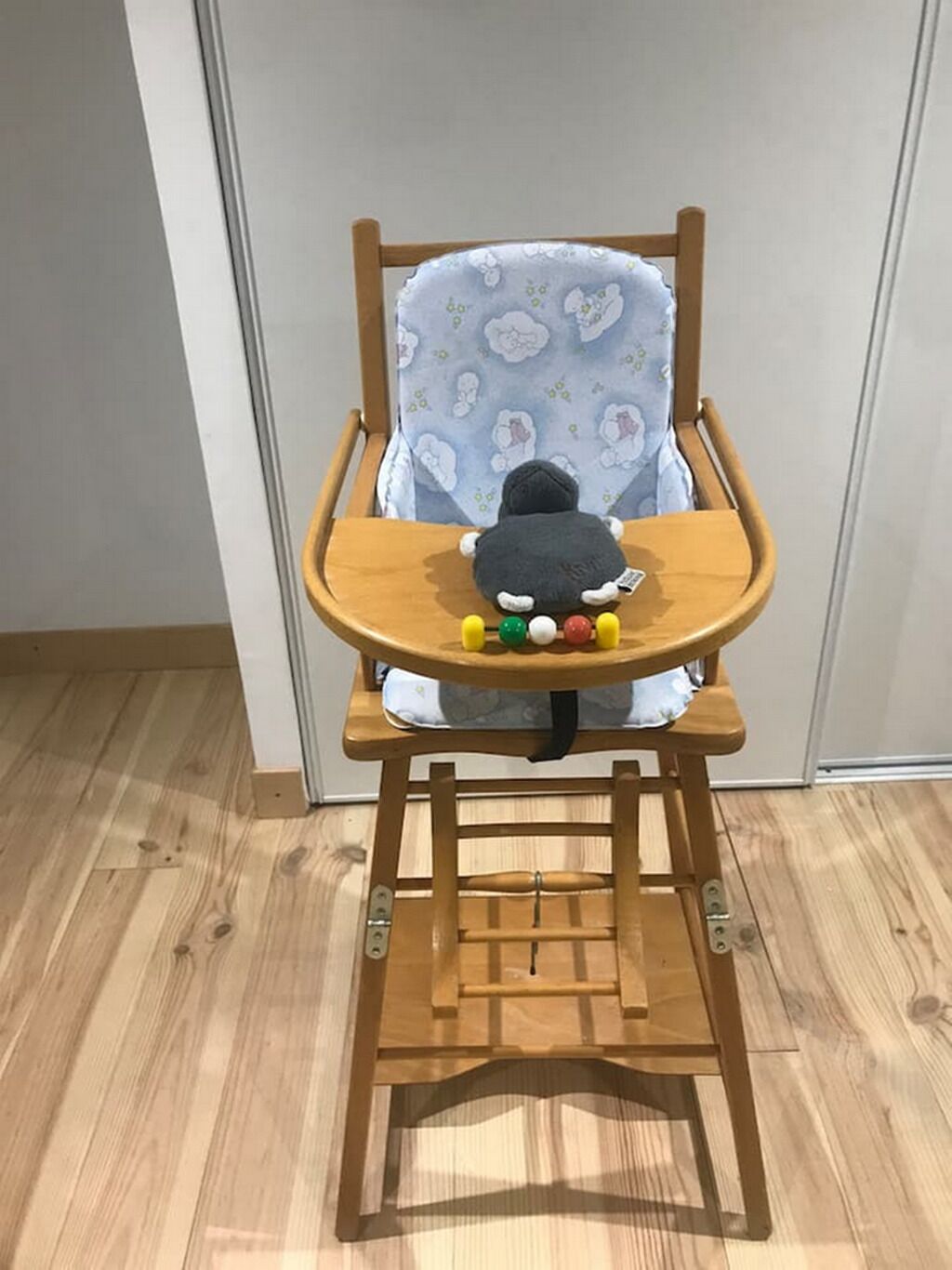 Une chaise haute en bois avec un coussin à motifs bleus et un jouet en peluche posé sur le plateau.