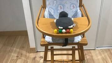 Une chaise haute en bois avec un coussin à motifs bleus et un jouet en peluche posé sur le plateau.