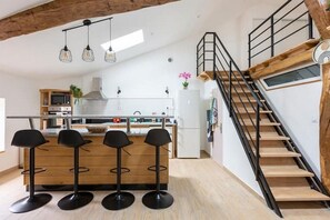 A modern kitchen with a central island, bar stools, a staircase, and a wooden ceiling. - Close to town center, 11 minutes from Center Parc. Mezzanine and children's play area. (Casteljaloux)