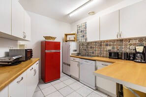 Una cocina compacta con gabinetes blancos, un refrigerador rojo, un lavavajillas y una encimera de madera.