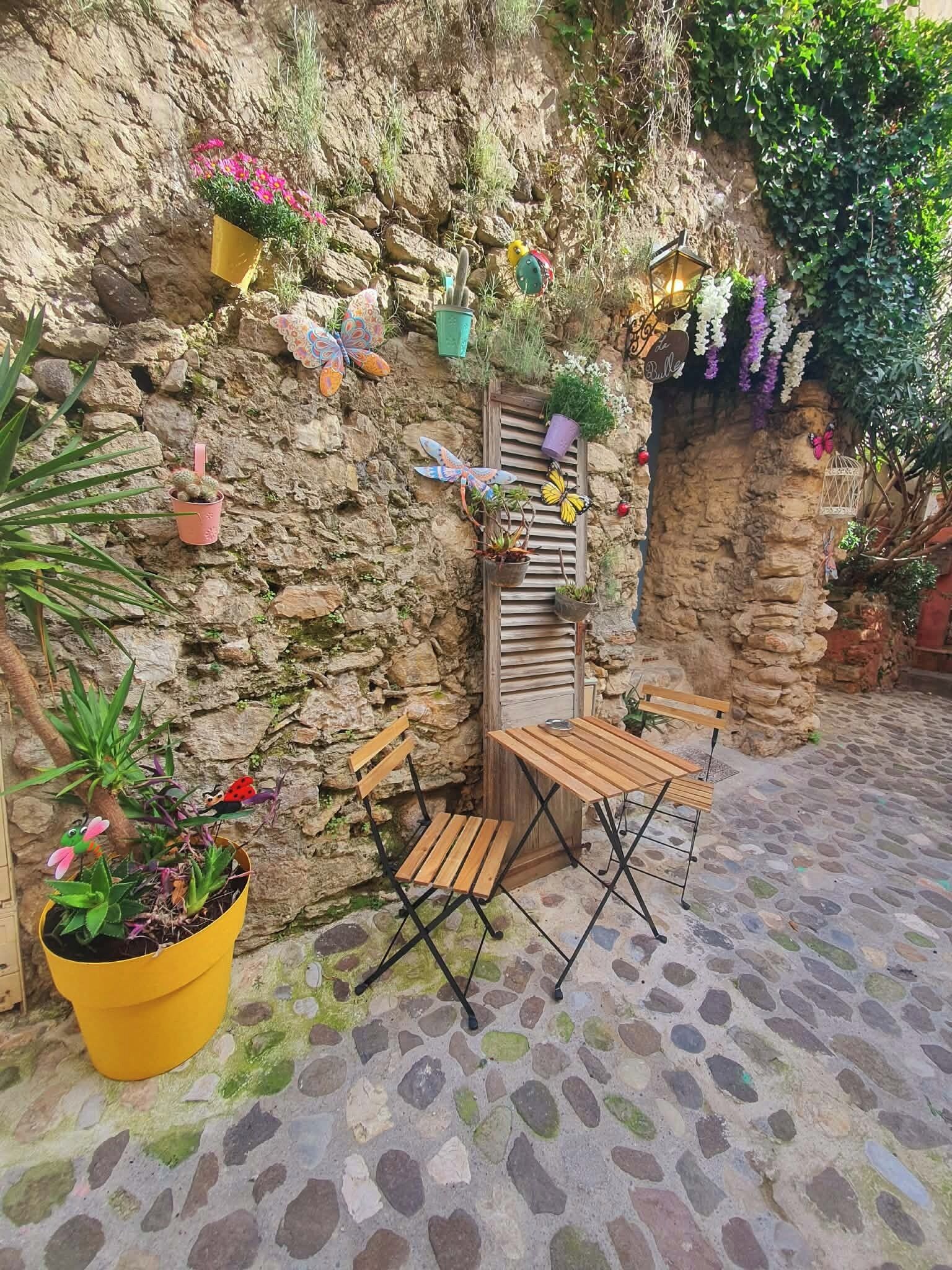 A stone patio with a wooden table and chairs, surrounded by potted plants and decorative butterflies.