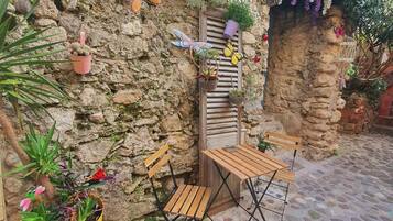 A stone patio with a wooden table and chairs, surrounded by potted plants and decorative butterflies.
