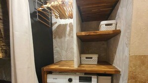A compact laundry room with a front-loading washing machine, wooden shelves, and a hanging rack. - La Bulle, an authentic and romantic spa (Biot)