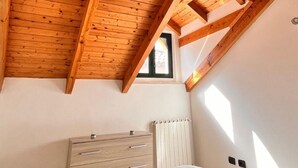 A bedroom with a sloped wooden ceiling, a window, a radiator, and a bed with a checkered bedspread. - Hostpitaly   La Quiete in Centro (CHIVASSO)