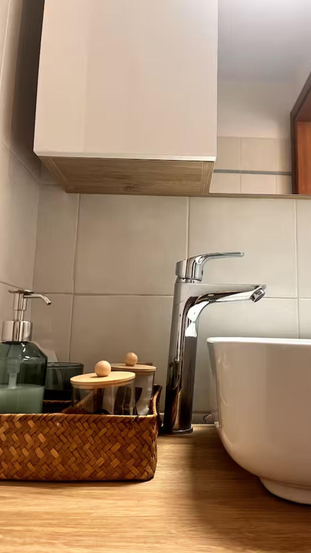 Een badkamer met een witte wastafel, een chromen kraan en een houten kast erboven.