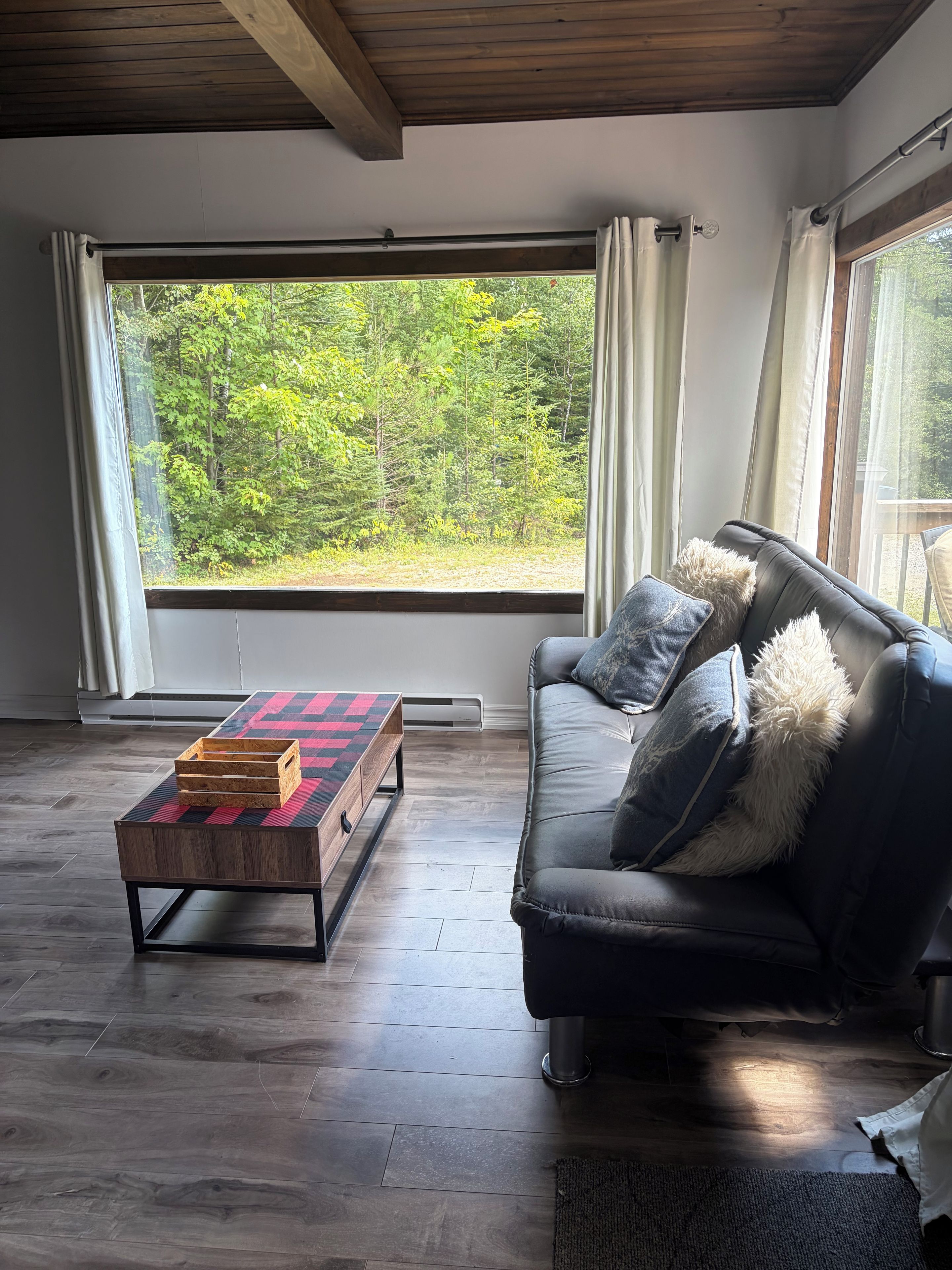 Ein modernes Wohnzimmer mit einem großen Fenster, einem dunklen Ledersofa und einem Couchtisch aus Holz.