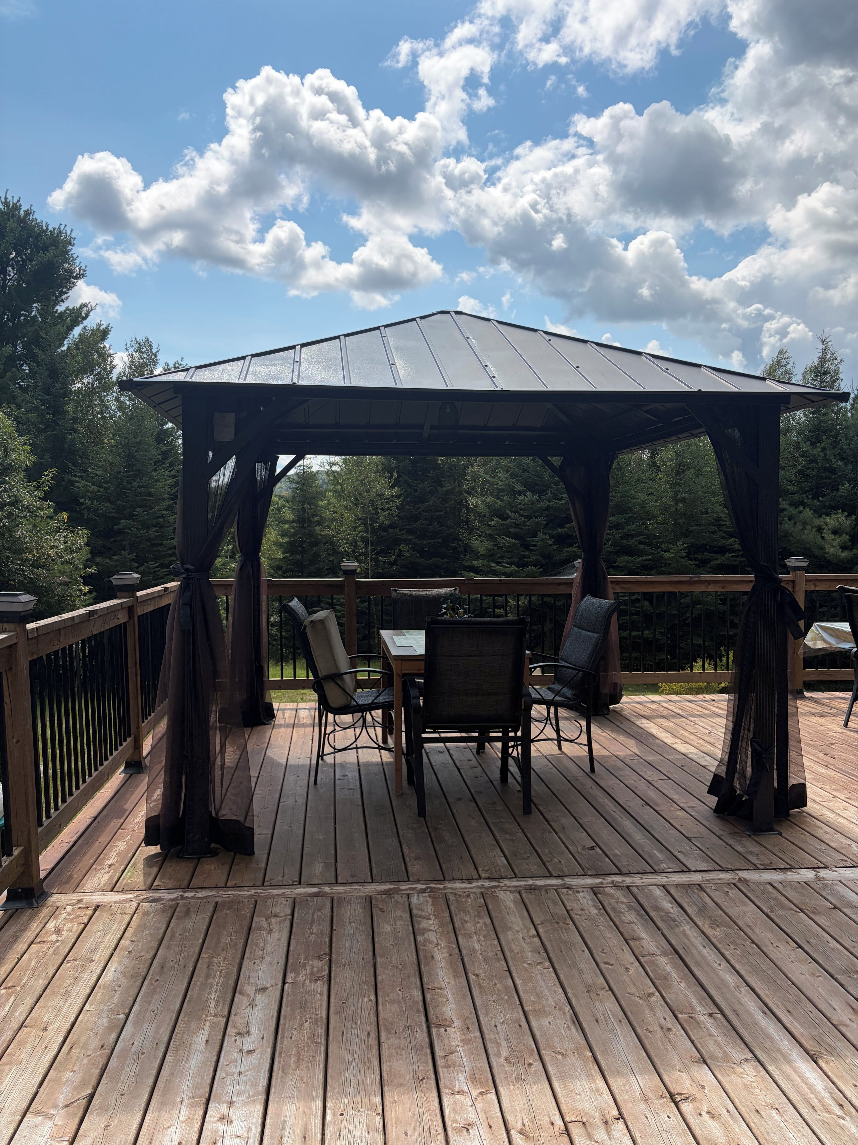 A wooden deck with a gazebo, outdoor furniture, and a railing.