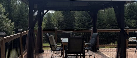 A wooden deck with a gazebo, outdoor furniture, and a railing.