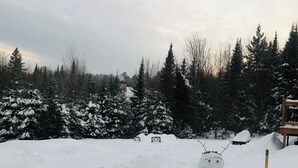 A snowman in a snowy outdoor area with trees and a wooden structure in the background. - Le petit chalet Chertsey (Chertsey)