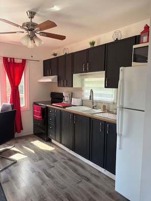 A modern kitchen with dark cabinets, a white refrigerator, and a ceiling fan. - The Little Chalet in Chertsey (Chertsey)