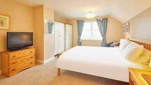 A hotel room with a large bed, a television on a wooden dresser, a wardrobe, and a window with curtains. - Host & Stay | Amberleigh (North Sunderland)