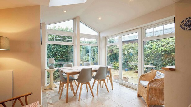 A bright dining area with a table and chairs, large windows, and a wicker chair. - Host & Stay | Amberleigh (North Sunderland)