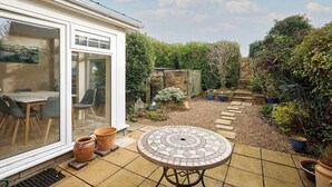 A patio with a tiled table, potted plants, and a glass door leading to an indoor area with a table and chairs. - Host & Stay | Amberleigh (North Sunderland)
