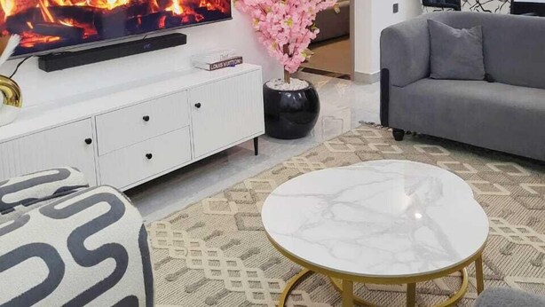 A modern living room with a flat-screen TV, a fireplace, a sofa, a coffee table, and decorative plants. - Golden Mango Heights Apartments (Nairobi)