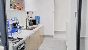 A modern kitchen with white cabinets, a gas stove, a sink, and a blue dish rack. - Golden Mango Heights Apartments (Nairobi)