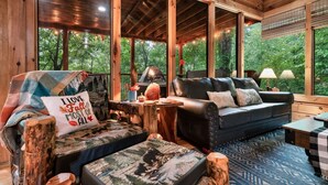 L’intérieur d’un chalet accueillant, avec un plafond en bois, un canapé en cuir, une couverture à carreaux et un coussin orné d’un motif sur le thème de la forêt.