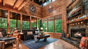 Un intérieur de chalet chaleureux avec une cheminée, des murs en bois, de grandes fenêtres et un coin salon confortable.
