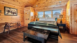 A log cabin bedroom with a bed, a bench, a table, and a picture on the wall. - 4BR w/Mountain Views! Hot Tub*Game Room*Comm Pool (Sevierville)