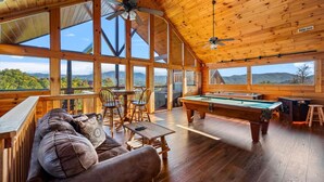 A spacious room with a pool table, a sofa, and a dining area with chairs. Large windows offer views of the outdoors. - 4BR w/Mountain Views! Hot Tub*Game Room*Comm Pool (Sevierville)