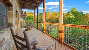A wooden deck with chairs, a stone wall, and a view of trees and a cabin. - 4BR w/Mountain Views! Hot Tub*Game Room*Comm Pool (Sevierville)
