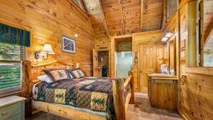 Un dormitorio de cabaña de madera con cama, mesita de noche, lámpara y vistas al exterior.