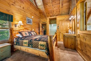 Un dormitorio de cabaña de madera con cama, mesita de noche, lámpara y vistas al exterior.